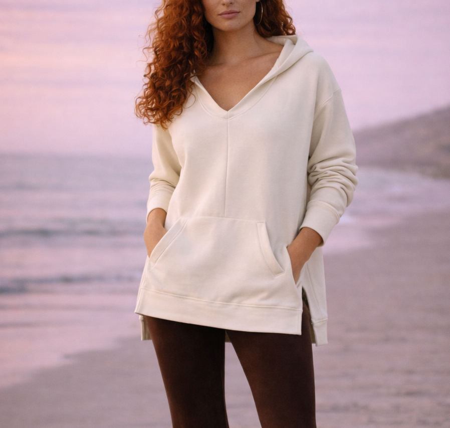 Person wearing a white hoodie and brown bell-bottom pants on a beach.